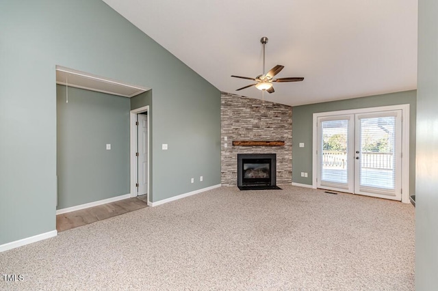 unfurnished living room with a ceiling fan, baseboards, carpet floors, attic access, and a stone fireplace