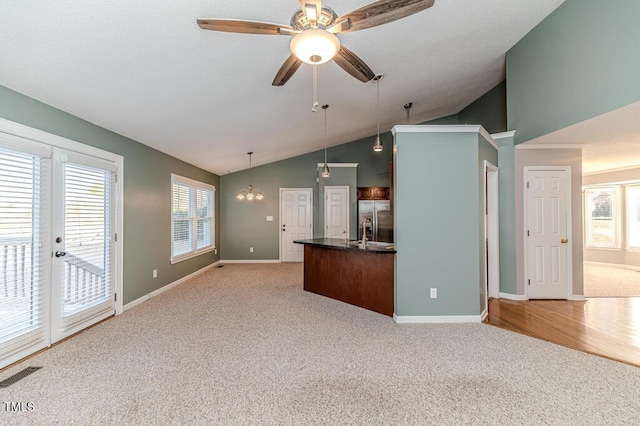 unfurnished living room with visible vents, baseboards, light colored carpet, vaulted ceiling, and ceiling fan with notable chandelier