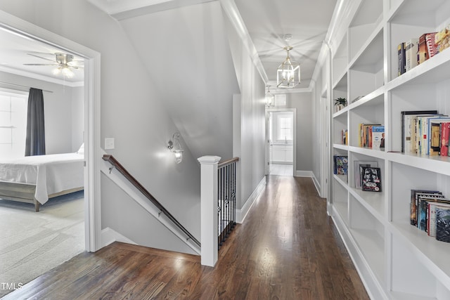 hall with an upstairs landing, built in shelves, ornamental molding, wood finished floors, and a chandelier