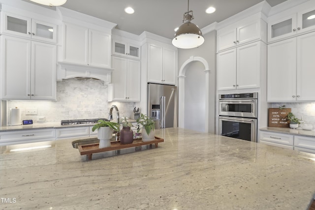 kitchen with light stone countertops, custom range hood, appliances with stainless steel finishes, white cabinetry, and tasteful backsplash