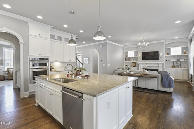 kitchen featuring arched walkways, a center island with sink, stainless steel appliances, and a sink