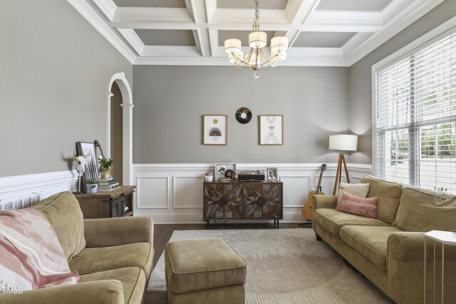 living area with beam ceiling, coffered ceiling, an inviting chandelier, and wainscoting