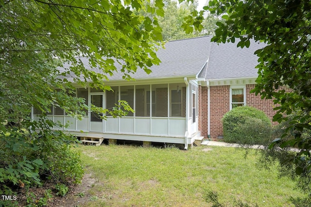 rear view of house with a yard, brick siding, a sunroom, and a shingled roof