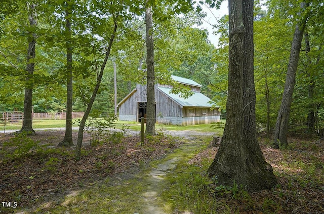 view of yard featuring fence, a wooded view, driveway, an outdoor structure, and a barn