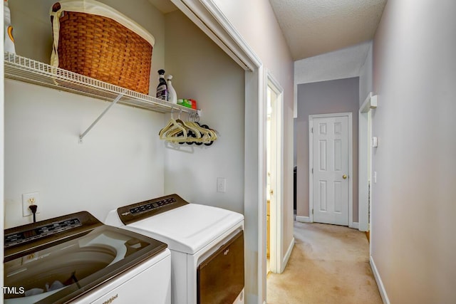 clothes washing area featuring washing machine and clothes dryer, baseboards, light colored carpet, laundry area, and a textured ceiling