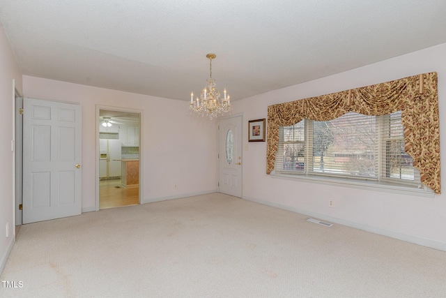 carpeted empty room with an inviting chandelier, baseboards, and visible vents