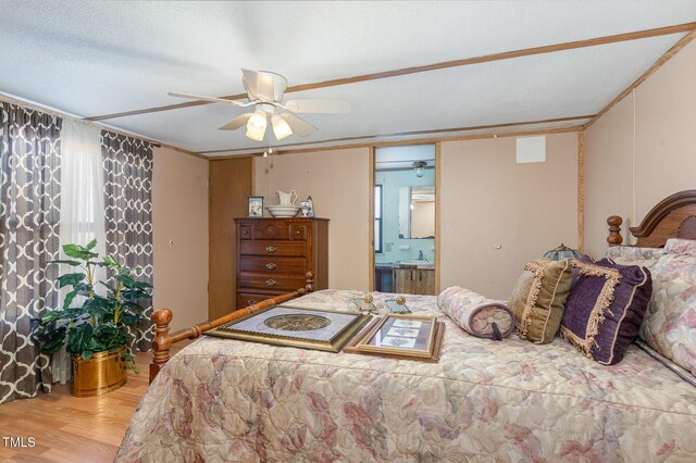 bedroom with ceiling fan, connected bathroom, a textured ceiling, and wood finished floors