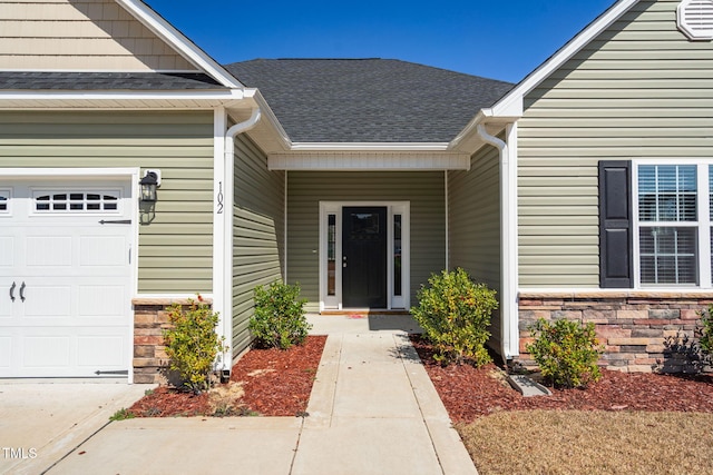 doorway to property with a garage, stone siding, and roof with shingles