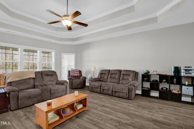 living area with baseboards, a raised ceiling, wood finished floors, and crown molding