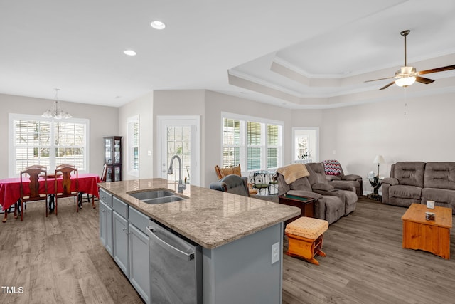 kitchen featuring light stone countertops, a center island with sink, light wood-style flooring, a sink, and stainless steel dishwasher