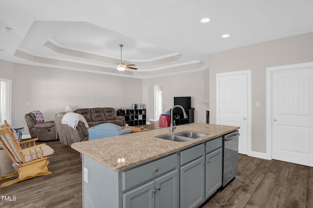 kitchen with dark wood finished floors, dishwasher, arched walkways, a raised ceiling, and a sink