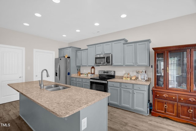 kitchen featuring light wood finished floors, a sink, light countertops, appliances with stainless steel finishes, and a kitchen island with sink