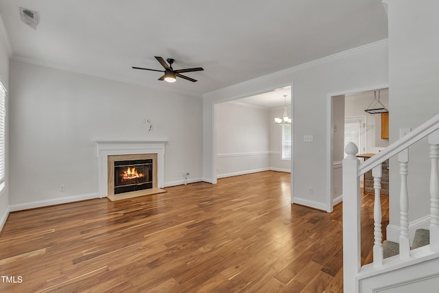 unfurnished living room with a fireplace with flush hearth, ornamental molding, ceiling fan with notable chandelier, wood finished floors, and stairs