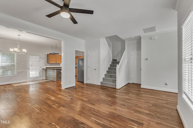 unfurnished living room with stairs, wood finished floors, visible vents, and ornamental molding