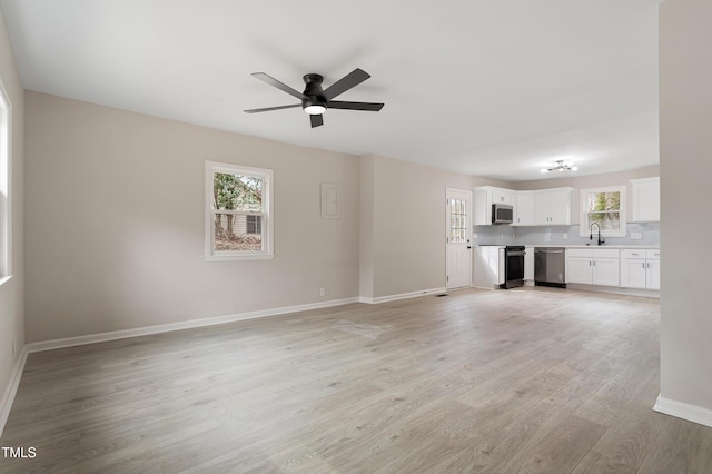 unfurnished living room featuring ceiling fan, light wood-style flooring, baseboards, and a sink