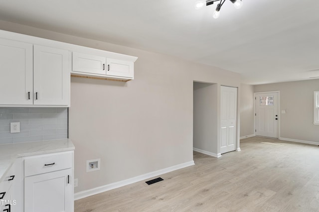 interior space featuring visible vents, baseboards, decorative backsplash, white cabinets, and light wood-style floors