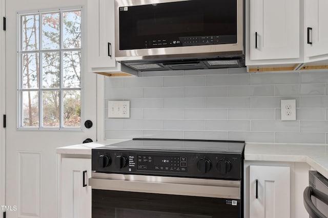 interior details featuring stainless steel microwave, white cabinetry, backsplash, and electric stove