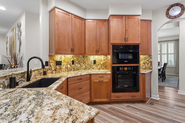 kitchen with light stone countertops, arched walkways, a sink, decorative backsplash, and light wood-style floors