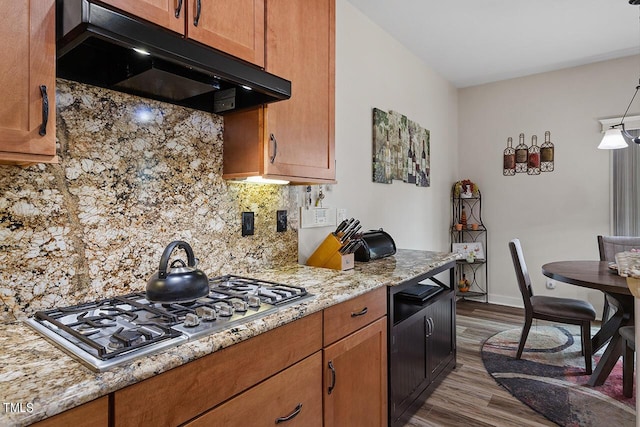 kitchen with light stone counters, wood finished floors, stainless steel gas cooktop, under cabinet range hood, and backsplash