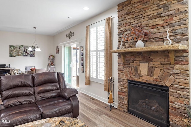 living room featuring a stone fireplace, baseboards, a healthy amount of sunlight, and wood finished floors