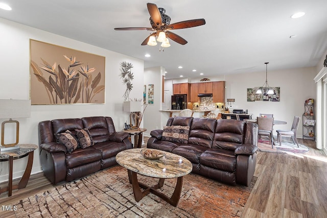 living room featuring ceiling fan with notable chandelier, recessed lighting, light wood-style floors, and baseboards