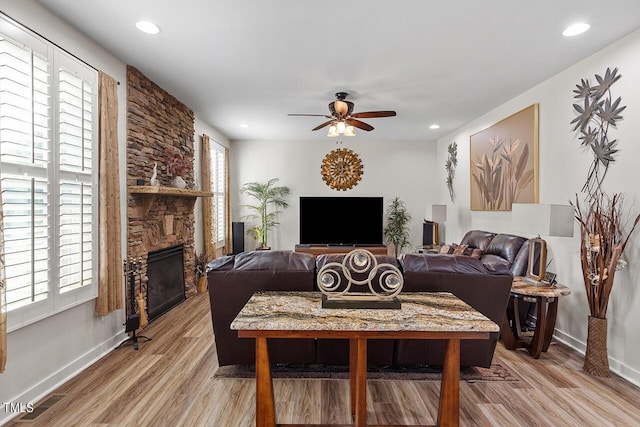 living area with a ceiling fan, a healthy amount of sunlight, a fireplace, and light wood finished floors