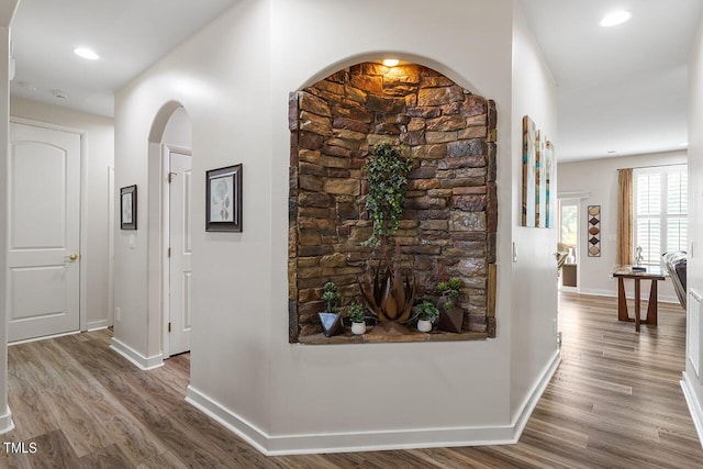 corridor with recessed lighting, wood finished floors, arched walkways, and baseboards