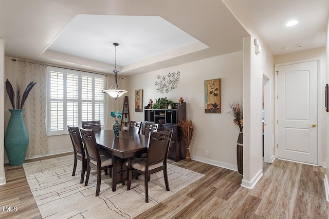 dining space featuring light wood-type flooring, a raised ceiling, and baseboards