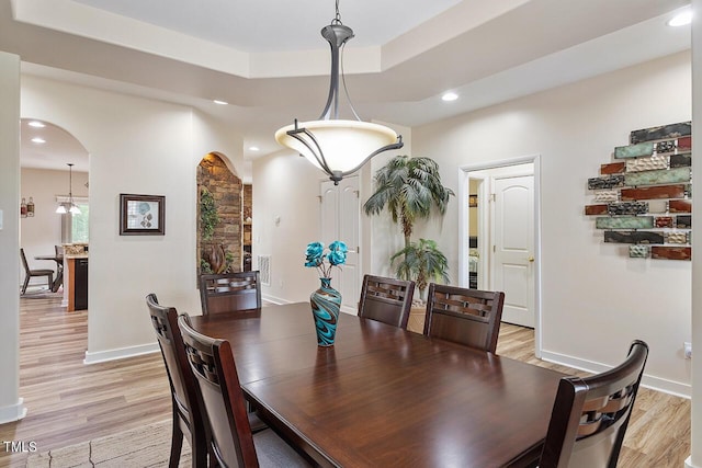 dining space featuring a tray ceiling, recessed lighting, arched walkways, light wood-style floors, and baseboards