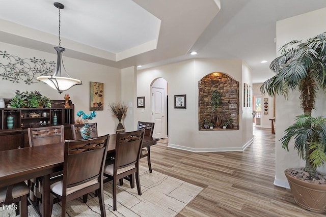 dining area with light wood-type flooring, recessed lighting, baseboards, arched walkways, and a raised ceiling