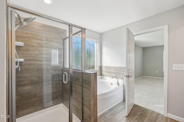 bathroom with a garden tub, wood finished floors, a stall shower, and baseboards