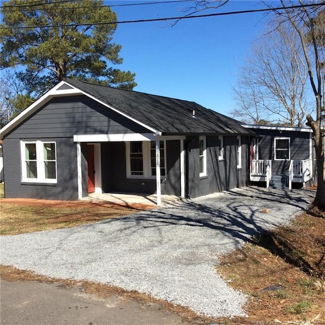 view of front facade with brick siding, gravel driveway, and covered porch