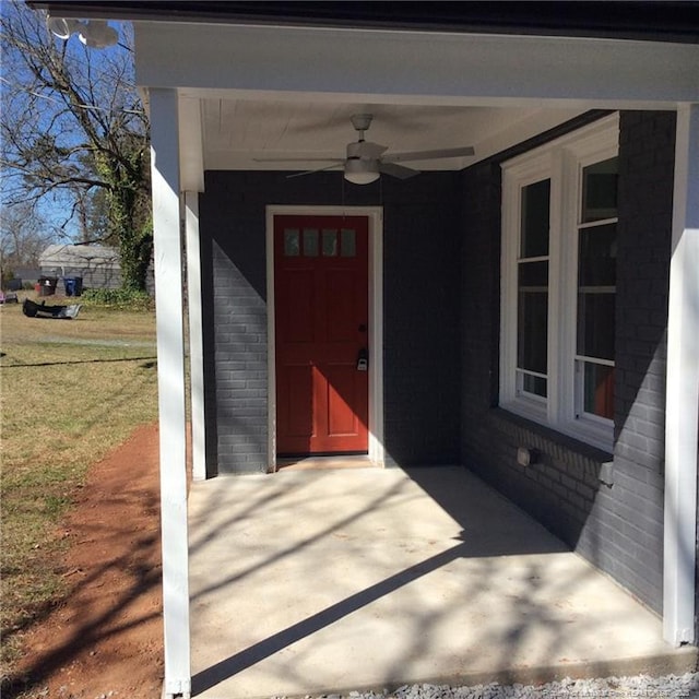 doorway to property featuring brick siding, a lawn, and a ceiling fan