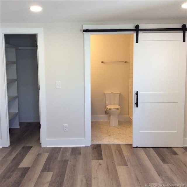 unfurnished bedroom with a walk in closet, wood finished floors, a barn door, a closet, and baseboards