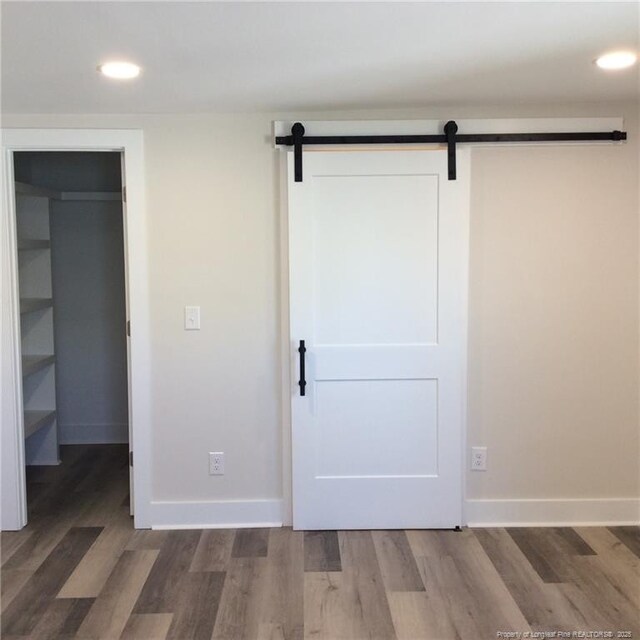 unfurnished bedroom with a barn door, wood finished floors, baseboards, and a walk in closet