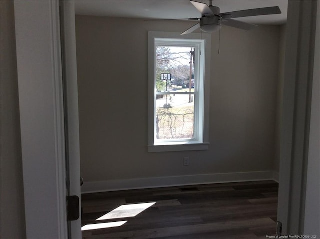 empty room featuring ceiling fan, baseboards, plenty of natural light, and dark wood-style floors