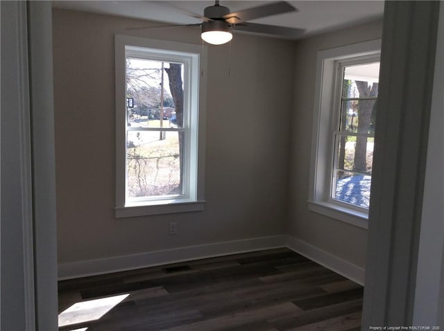 empty room with visible vents, a healthy amount of sunlight, dark wood-type flooring, and baseboards