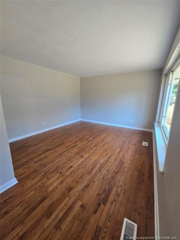 empty room with visible vents, baseboards, and dark wood-style flooring