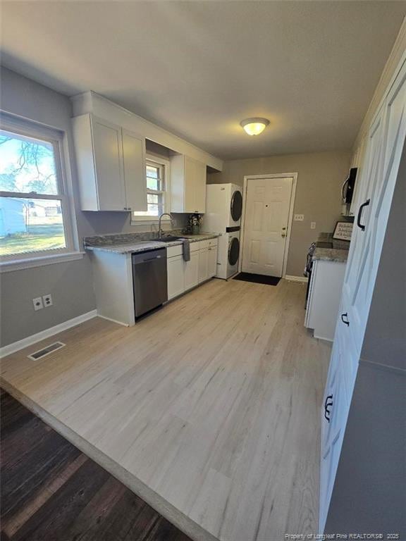 kitchen with visible vents, black dishwasher, white cabinetry, stainless steel stove, and stacked washer / dryer