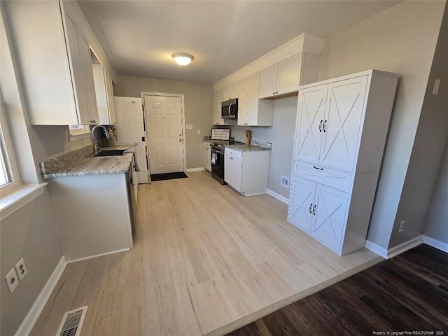 kitchen with stainless steel microwave, electric range, baseboards, and white cabinets