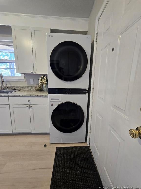 laundry area with cabinet space, stacked washer / drying machine, light wood finished floors, and a sink