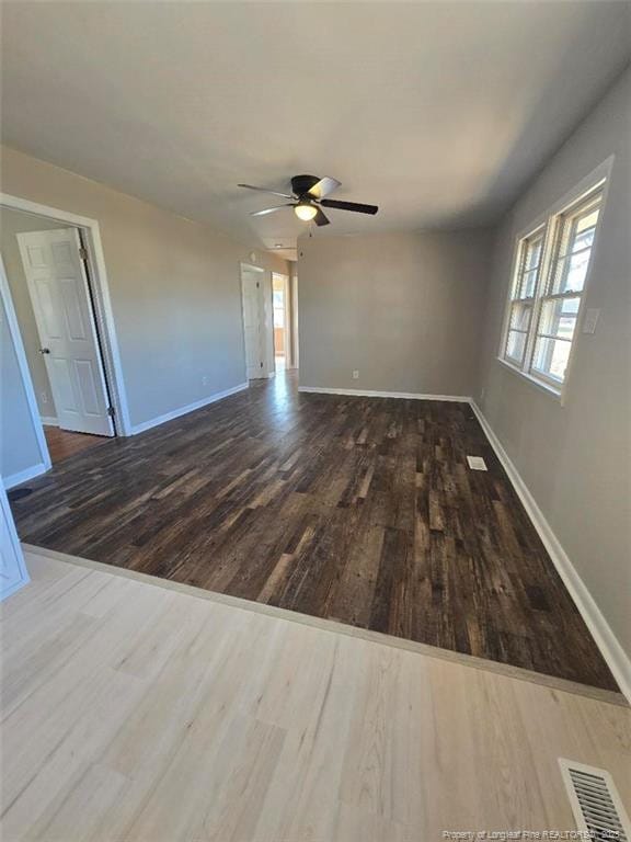 empty room with a ceiling fan, wood finished floors, visible vents, and baseboards