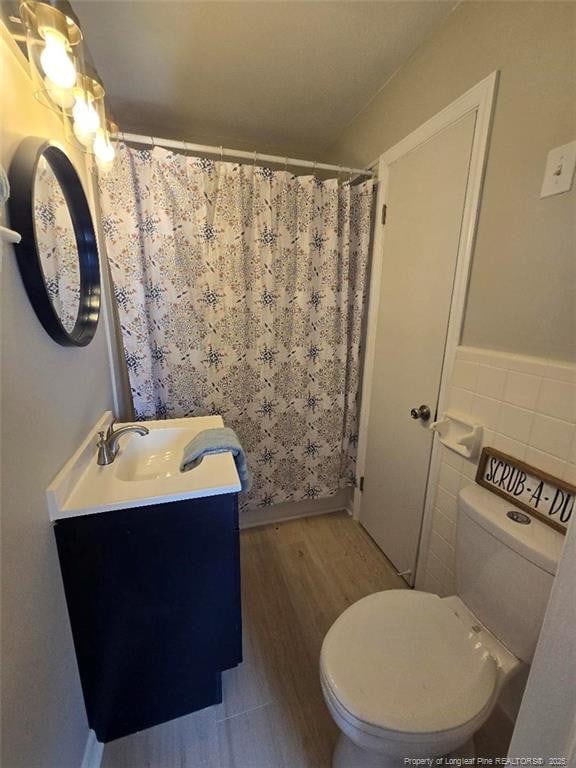 full bathroom featuring toilet, curtained shower, wood finished floors, tile walls, and vanity