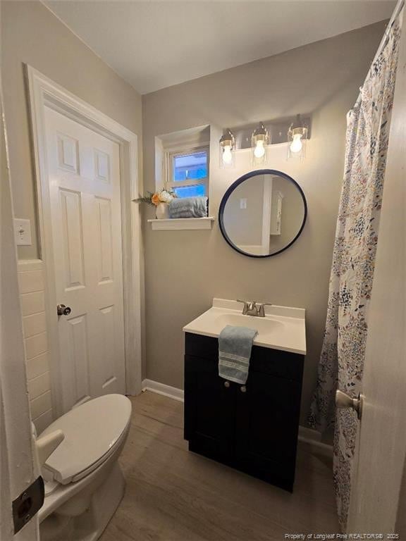 bathroom featuring baseboards, toilet, wood finished floors, and vanity