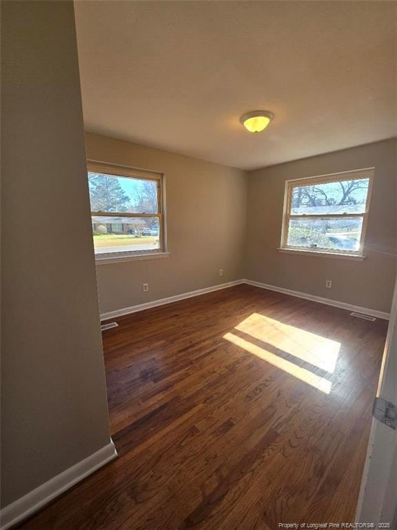 spare room featuring a wealth of natural light, baseboards, and dark wood finished floors