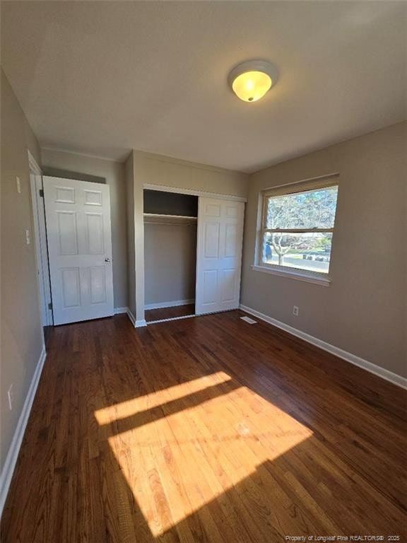 unfurnished bedroom featuring visible vents, baseboards, a closet, and dark wood-style flooring