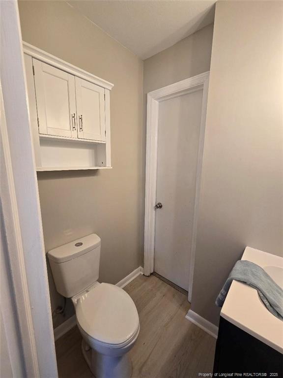 bathroom with toilet, vanity, baseboards, and wood finished floors