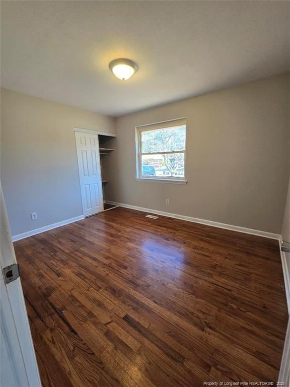 unfurnished bedroom featuring a closet, visible vents, baseboards, and dark wood-style flooring