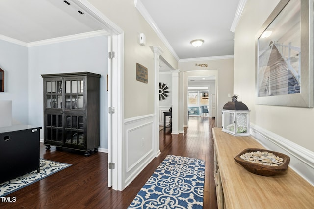 hall with crown molding, a wainscoted wall, decorative columns, a decorative wall, and dark wood-style flooring