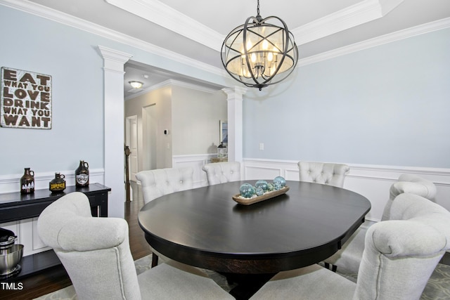 dining room with a tray ceiling, decorative columns, ornamental molding, wainscoting, and a chandelier